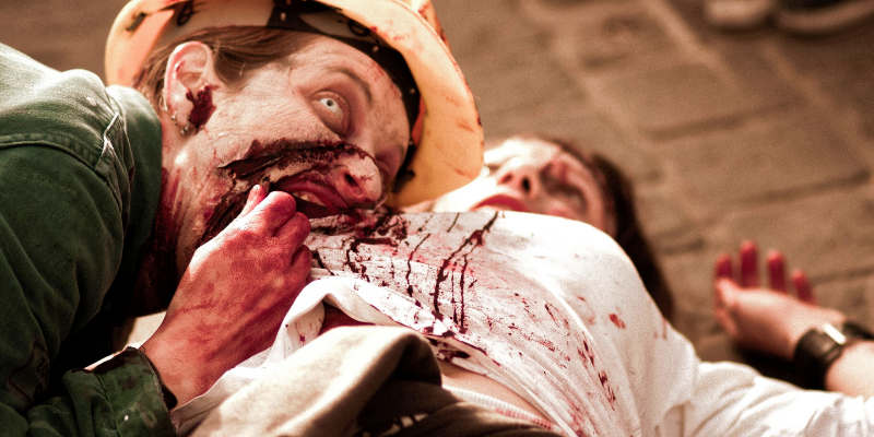 zombie looking up at camera with one eye while attacking a person eating their guts