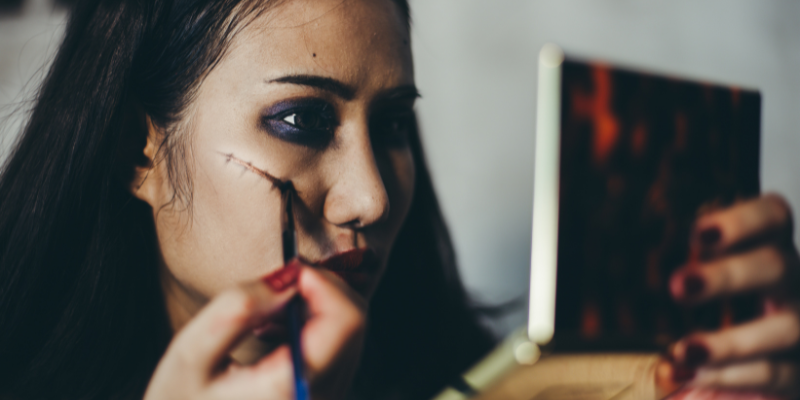 Woman looking in a mirror and putting on scary makeup