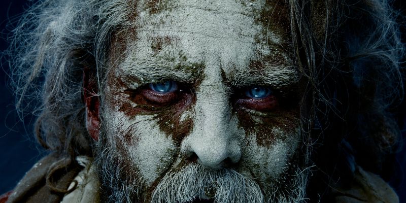 elderly man covered in clay and dirt with piercing blue eyes up close