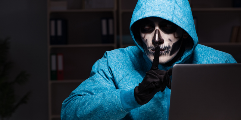 Man painted to look like skeleton whispering infront of a computer 