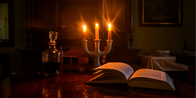 Candlelit room with a book and bottle on a table.