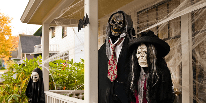 Three skeleton Halloween figures out on the porch of a house with spider webs.