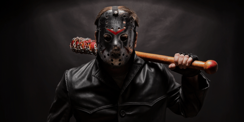 Man with a hockey mask carrying a bat with barbed wire wrapped around it.