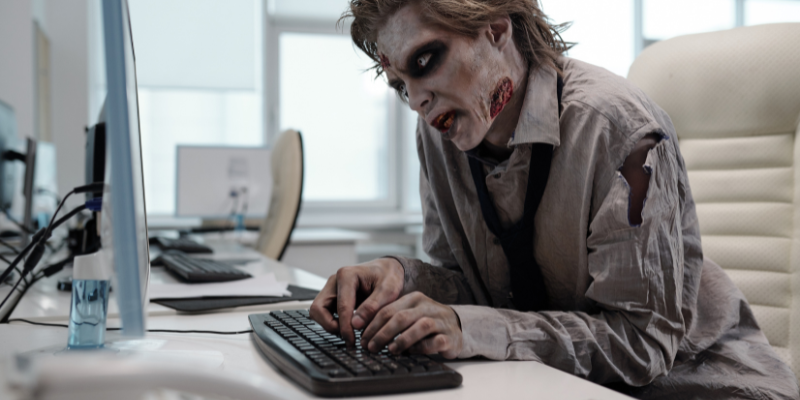 Ugly man with zombie makeup working at a computer in an office