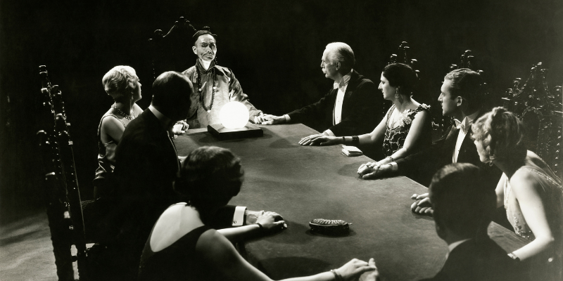 Black and white historical photos of a group of people in 1920s party attire gathered around a table for a seance