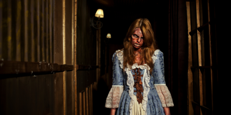 Demon young woman wearing a period dress with lace sleeves in a haunted hallway