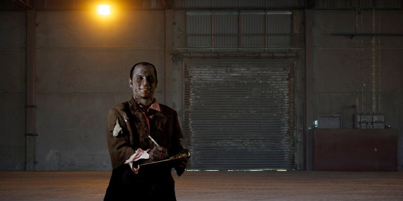 Smiling zombie holding a clipboard and pen standing in a spooky warehouse