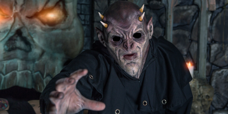 Horned demon reaching out to attack you in front of stone skull background