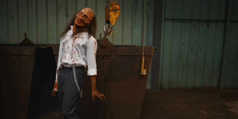 Balding zombie with long hair in the back wearing a bloody shirt in an abandoned factory