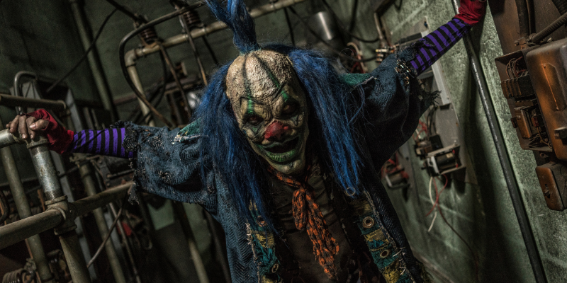 Creepy clown with blue hair approaching you in an industrial hallway