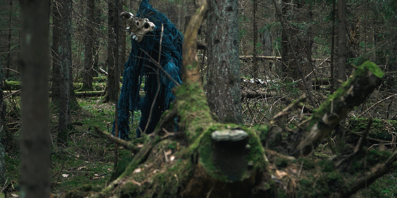 Terrible monster wearing blue rags standing among trees in a forest