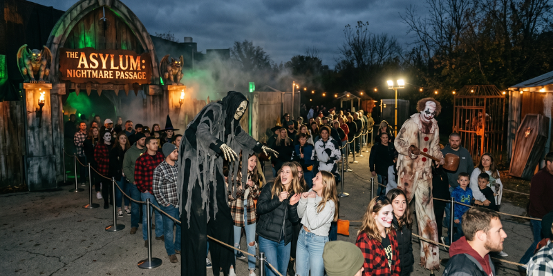 Exterior queue area of The Asylum_ Nightmare Passage with a long line of guests interacting with scare-actors while they wait to enter the attraction